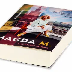 Okładka książki "Magda M. Ciąg dalszy nastąpił" z Radosławem Figurą. Uśmiechnięta Magda M. siedzi na krześle na tle panoramy miasta.