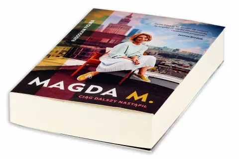 Okładka książki "Magda M. Ciąg dalszy nastąpił" z Radosławem Figurą. Uśmiechnięta Magda M. siedzi na krześle na tle panoramy miasta.