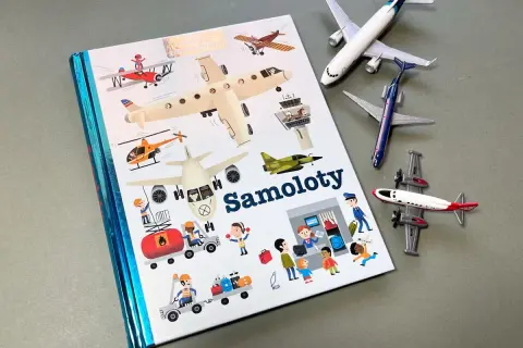 Książki o samolotach z ilustracjami różnych maszyn latających i ludzi pracujących na lotnisku. Obok leżą modele samolotów.