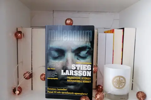Książka "Mężczyźni, którzy nienawidzą kobiet" Stiega Larssona na półce, ozdobionej migoczącymi lampkami.